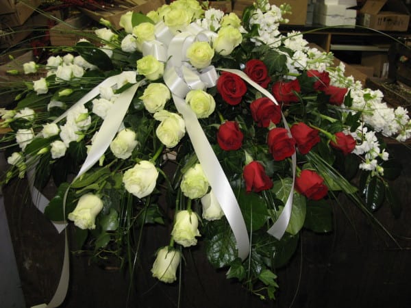 Red and white rose casket spray with white bow and trailing ribbons