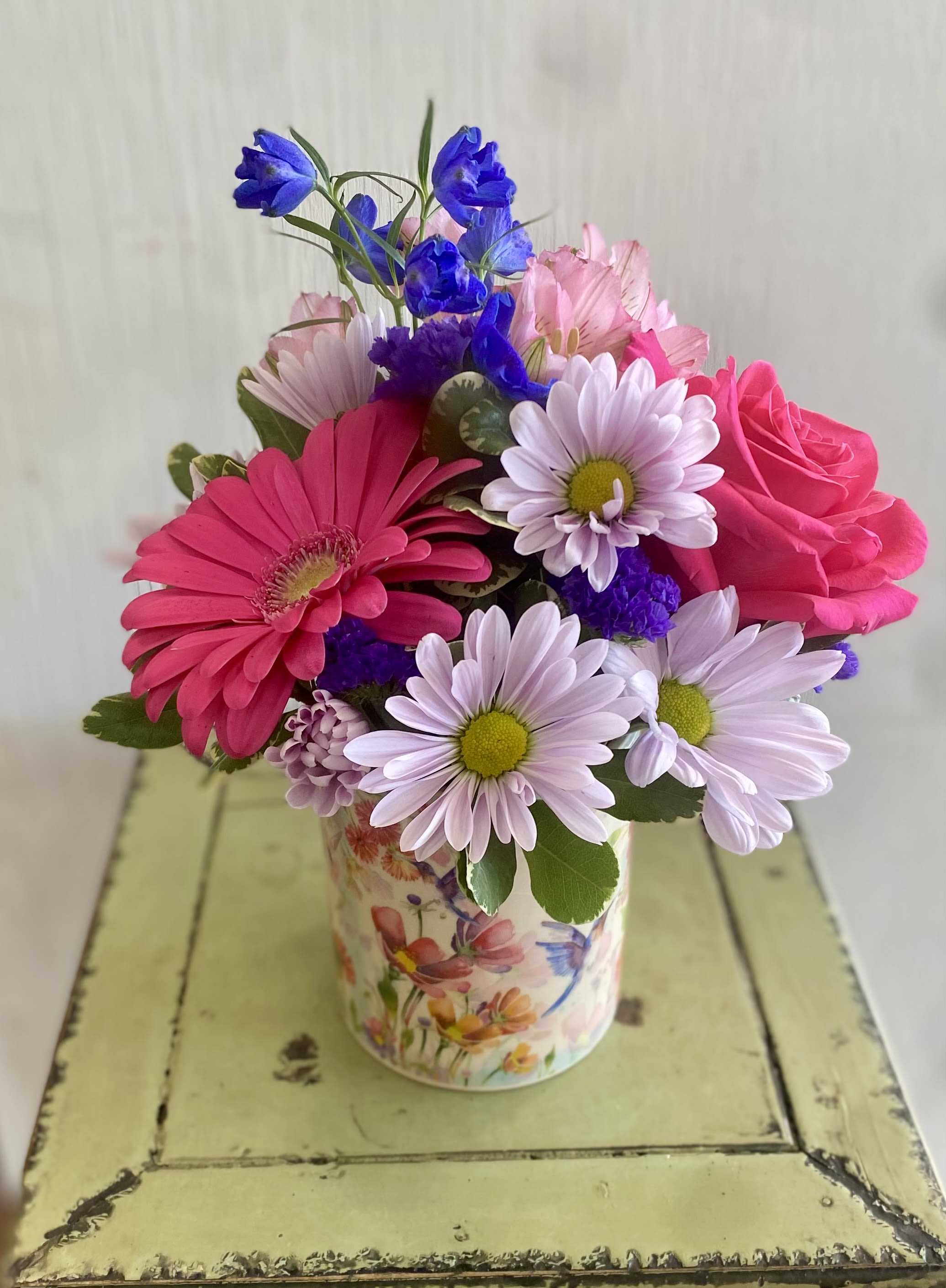 Mixed pink and purple flowers in a floral tin vase