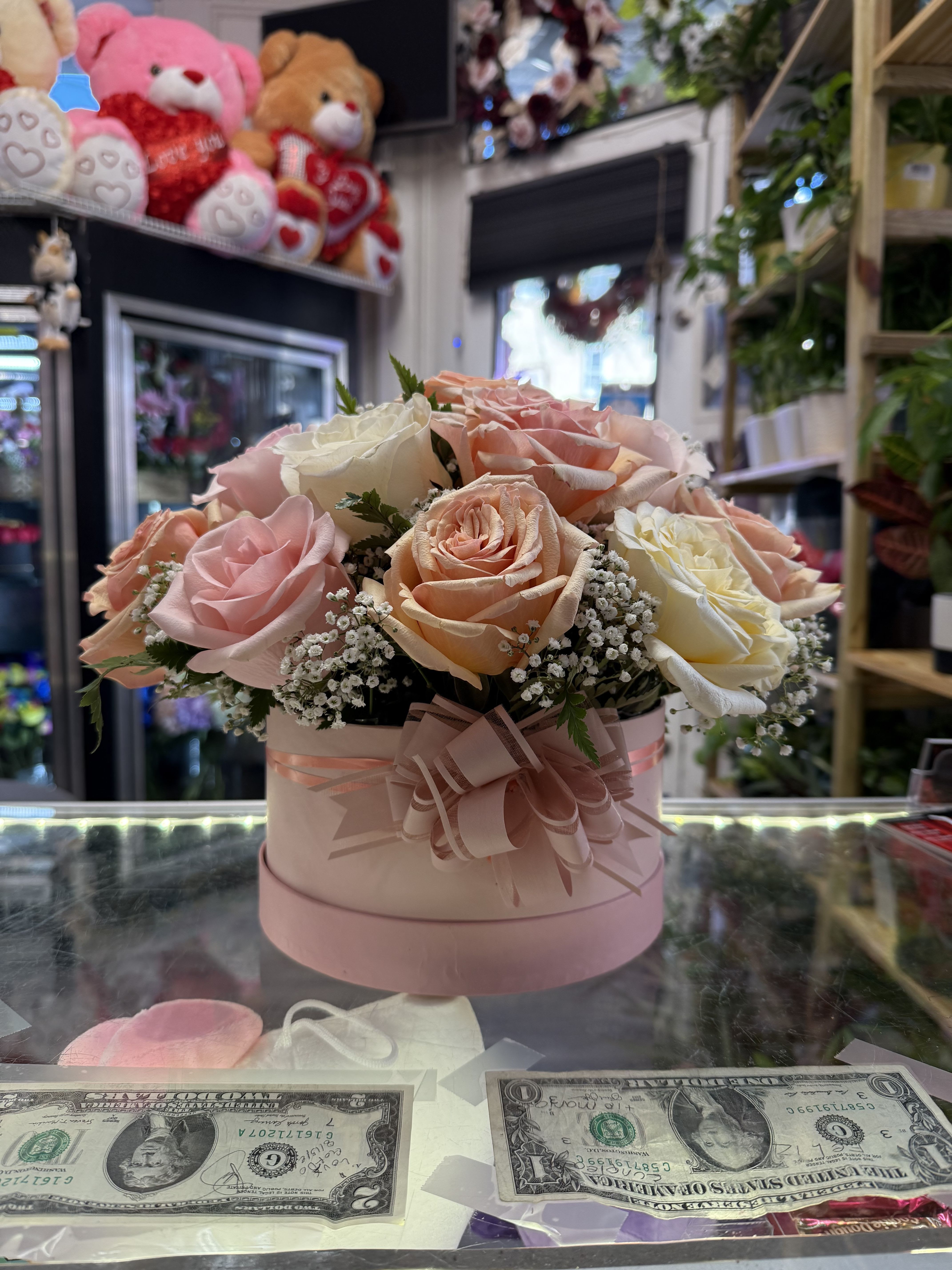 Pink and peach roses arranged in a round pink box with a ribbon bow