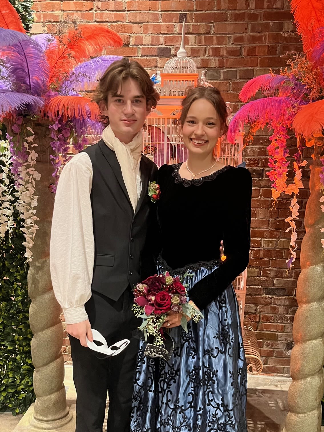 Young couple posing with a small red rose bouquet at a formal event