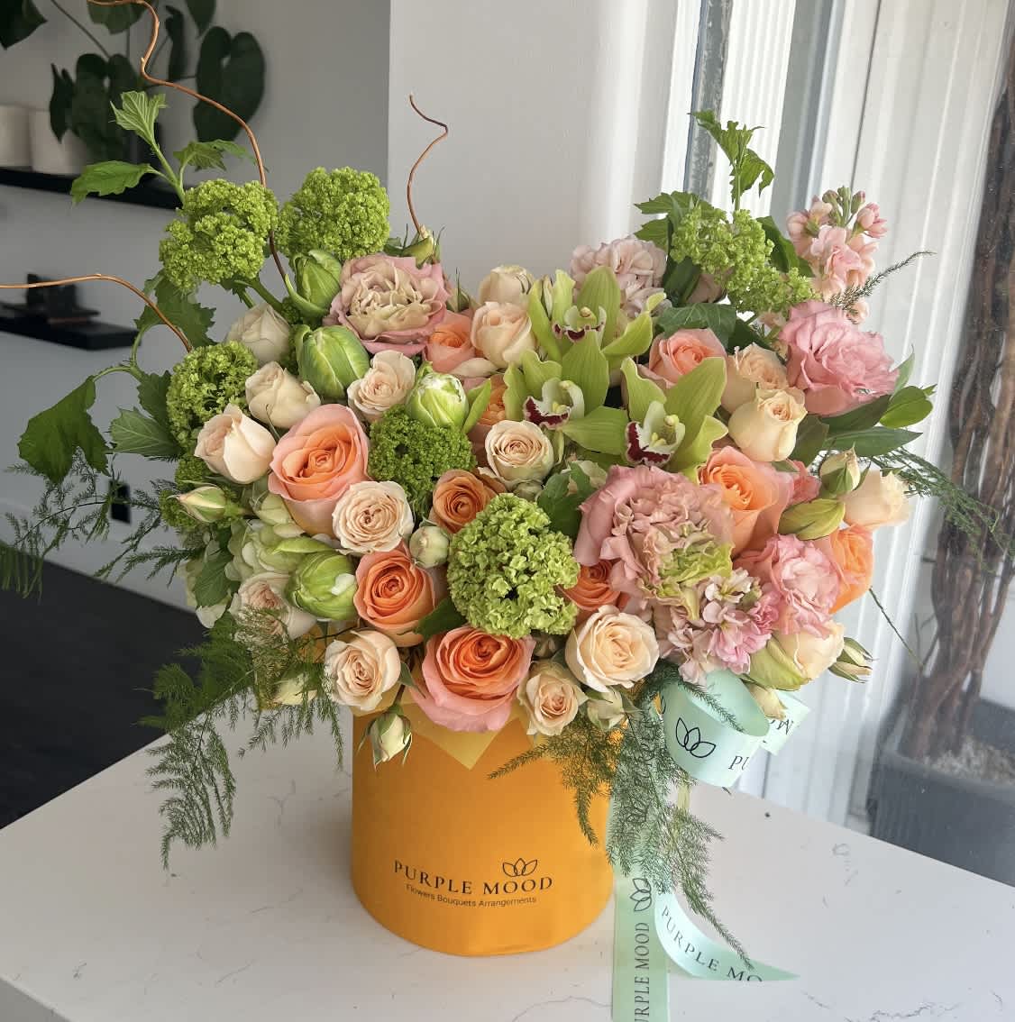 Mixed bouquet of peach and pink roses with green blooms in an orange hatbox