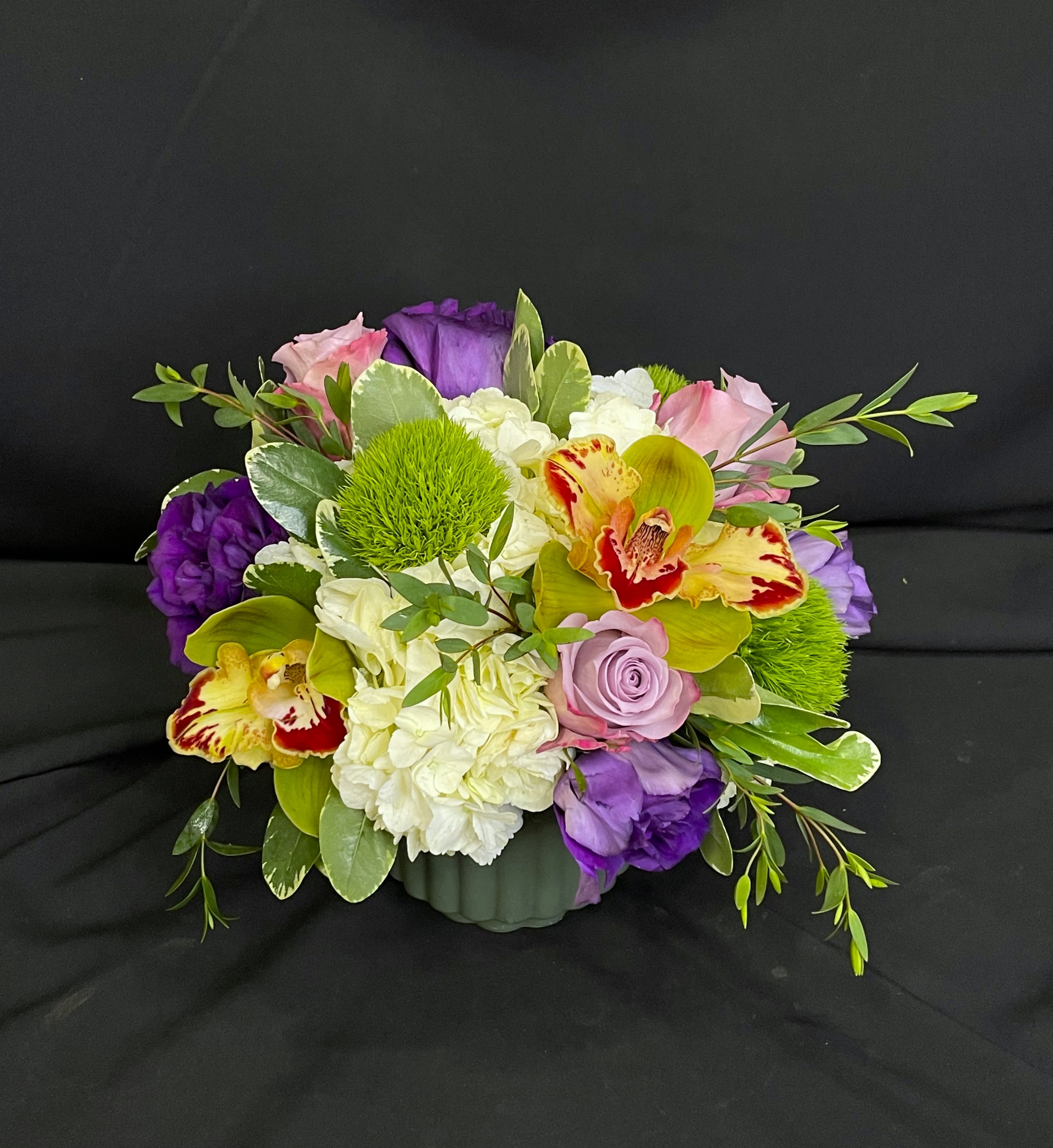 Olivia - Olivia is fresh fun and flirty! In a dark green ceramic vase, she stuns with purples greens and whites to create a moody arrangement that emulates nature. Standard and deluxe versions are about 10 inches tall and the premium goes in a larger vase.