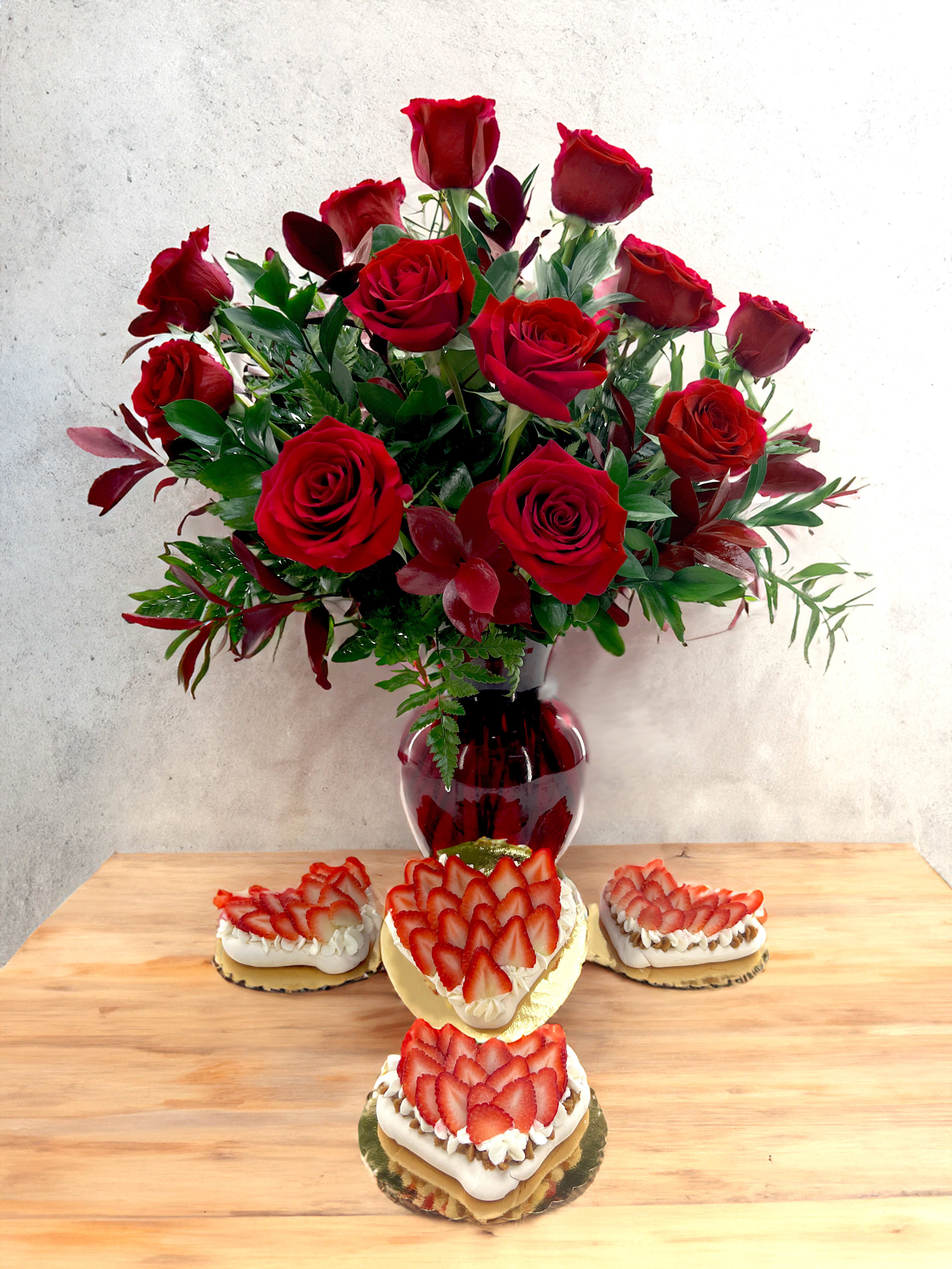 Red rose bouquet in a red vase with strawberry-topped desserts on a table