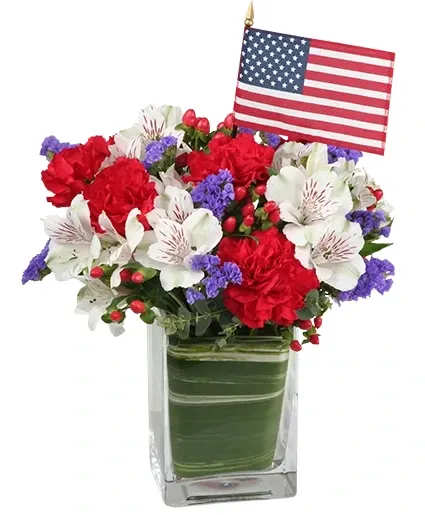 Made In The USA Patriotic Arrangement - Send Blooms Bursting in Air! This Red, White and Blue flower arrangement features a small American flag and lots of patriotic appeal for a great Summer pick-me-up! Call and order a vase of bright summer blooms for someone special or order flowers online 24/7.  Includes: Rectangular Vase , Foliage: Variegated Aspidistra Leaf , Red Grand Slam Carnations, White Virginia Alstroemeria, Blue Statice , Red Hypericum , Miniature American Flag.