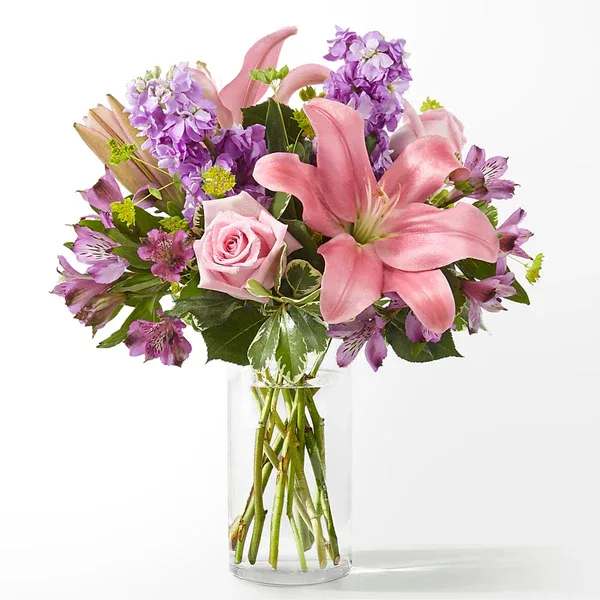 Pink lilies and roses with purple flowers in a clear glass vase