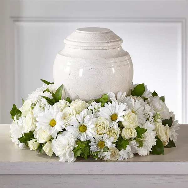 White funeral urn surrounded by white daisies and roses