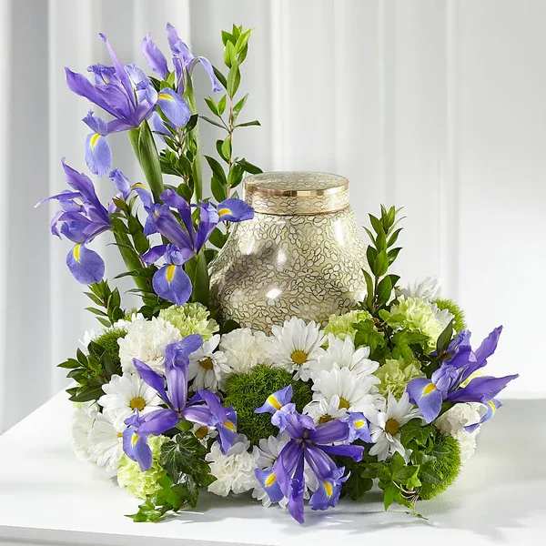 Purple irises and white daisies arranged around a decorative urn