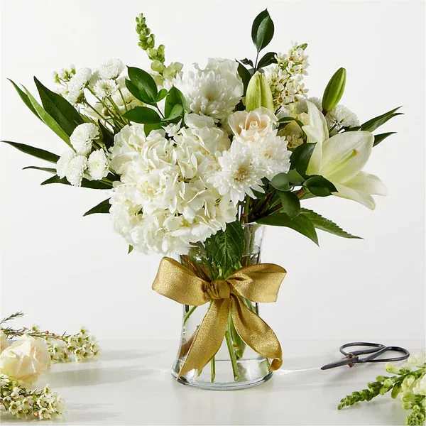 White floral bouquet in a clear glass vase with a gold ribbon