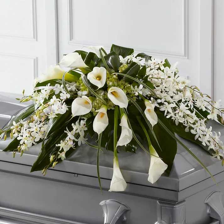 White calla lilies and orchids arranged on a gray casket