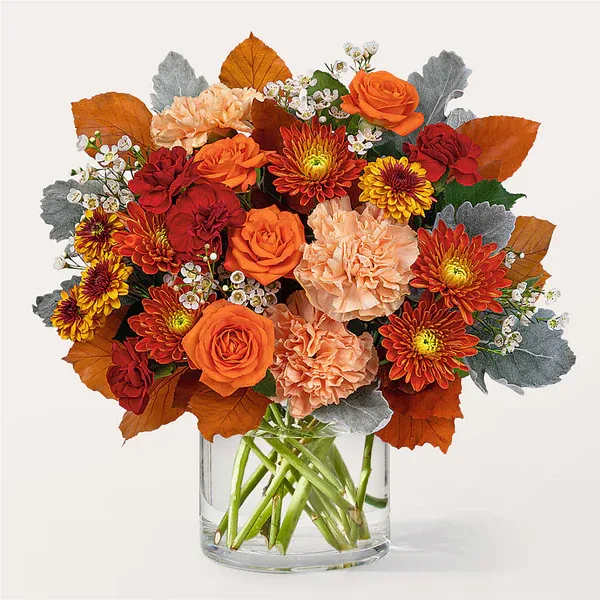 Orange and red bouquet with roses, carnations, and mums in a clear glass vase