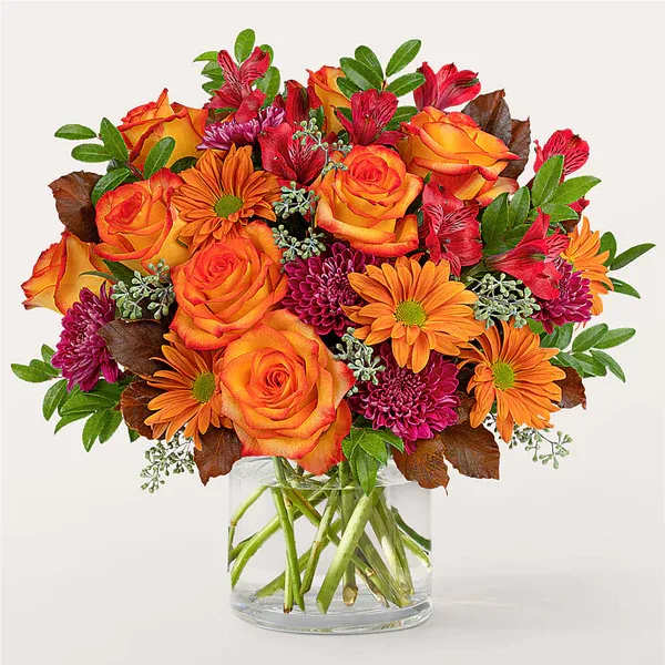 Orange roses and daisies in a clear glass vase