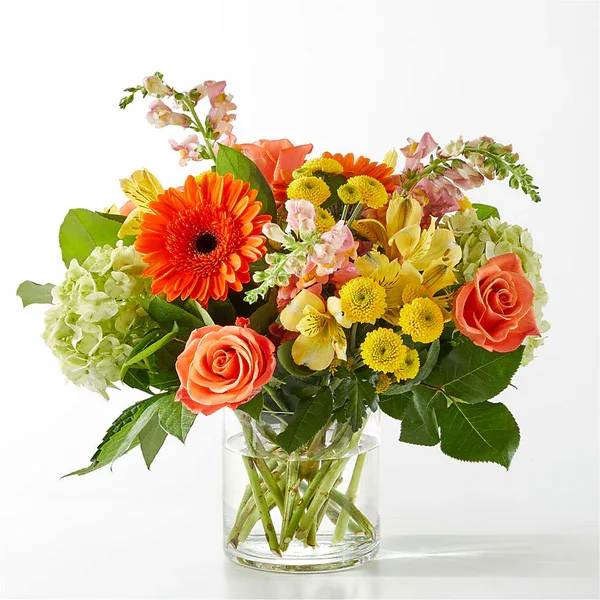 Mixed bouquet of orange roses, gerbera daisies, and yellow blooms in a glass vase