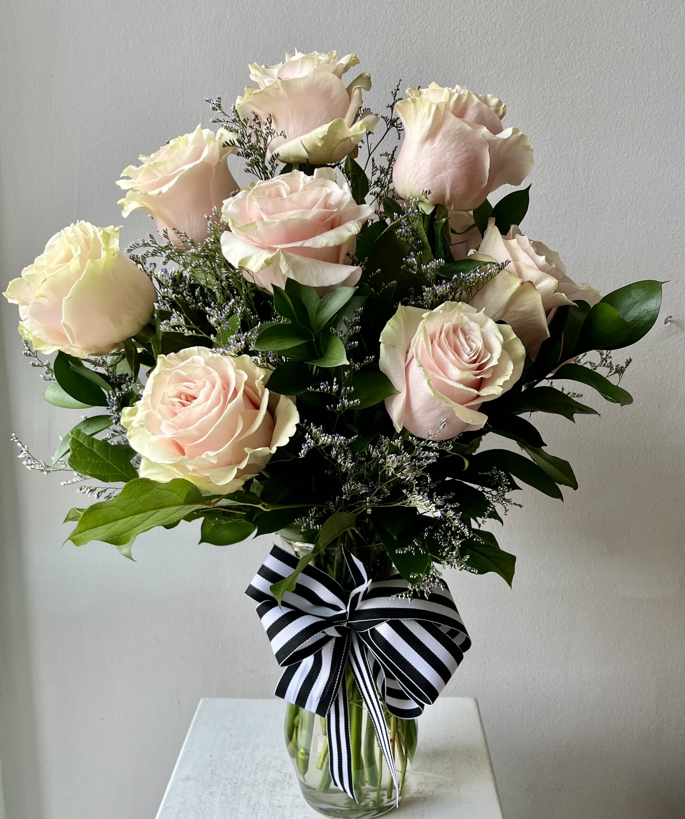 Bouquet of pale pink roses in a clear glass vase with a striped ribbon