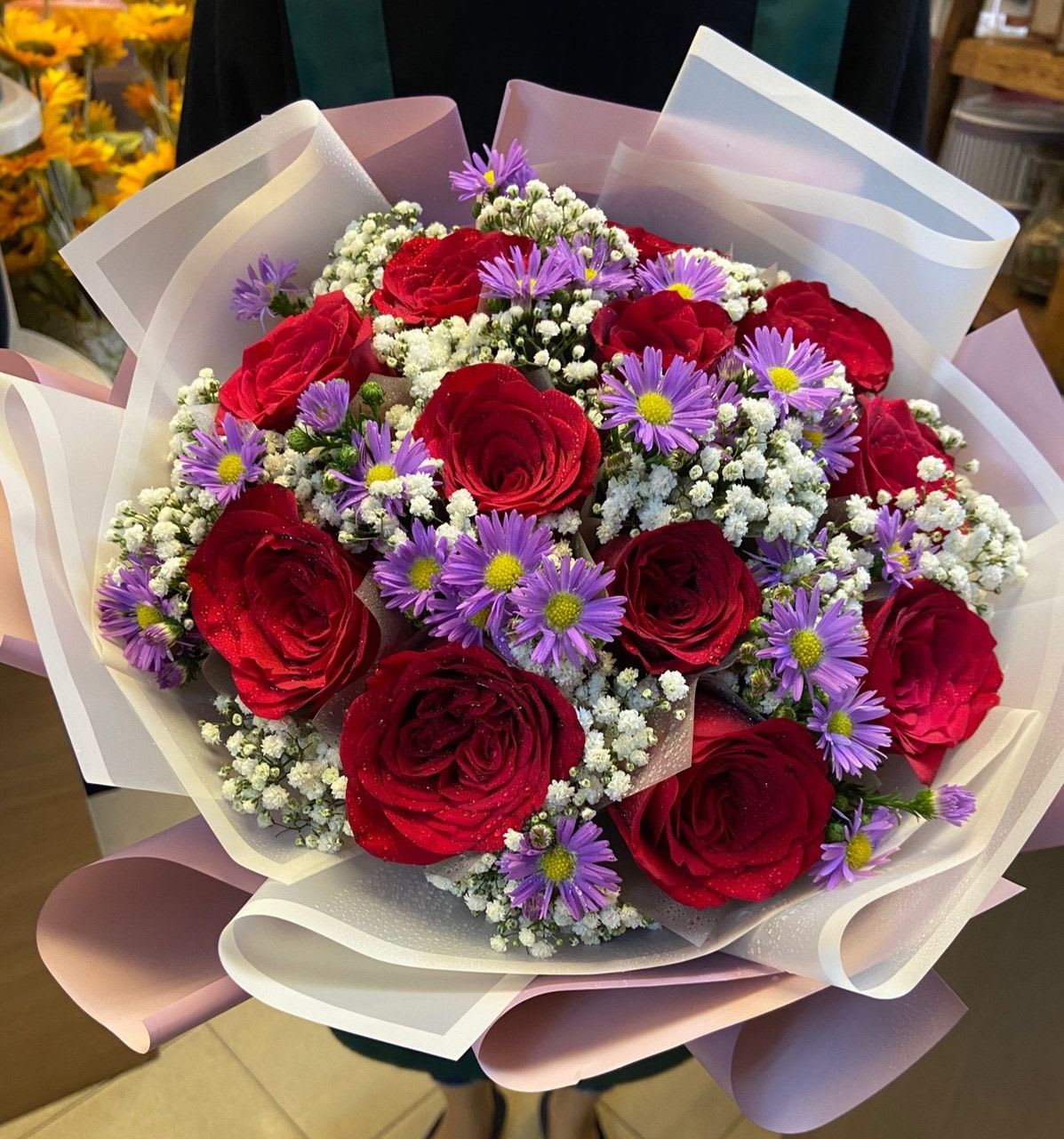Bouquet of red roses and purple daisies wrapped in white paper