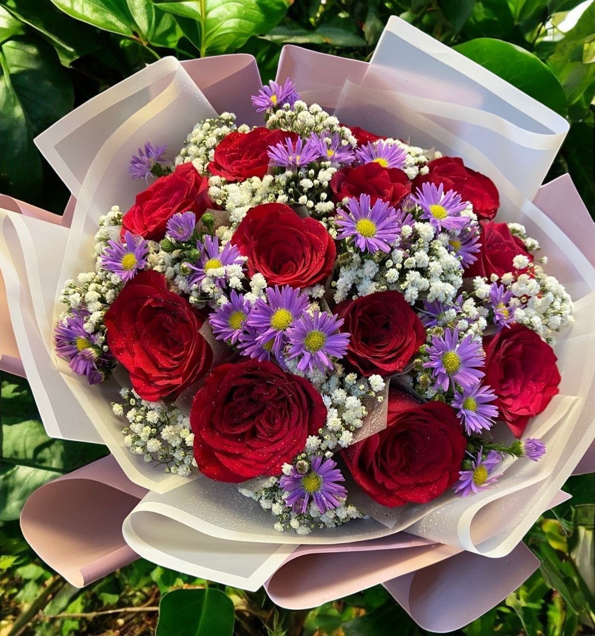 Bouquet of red roses and purple daisies wrapped in pale paper