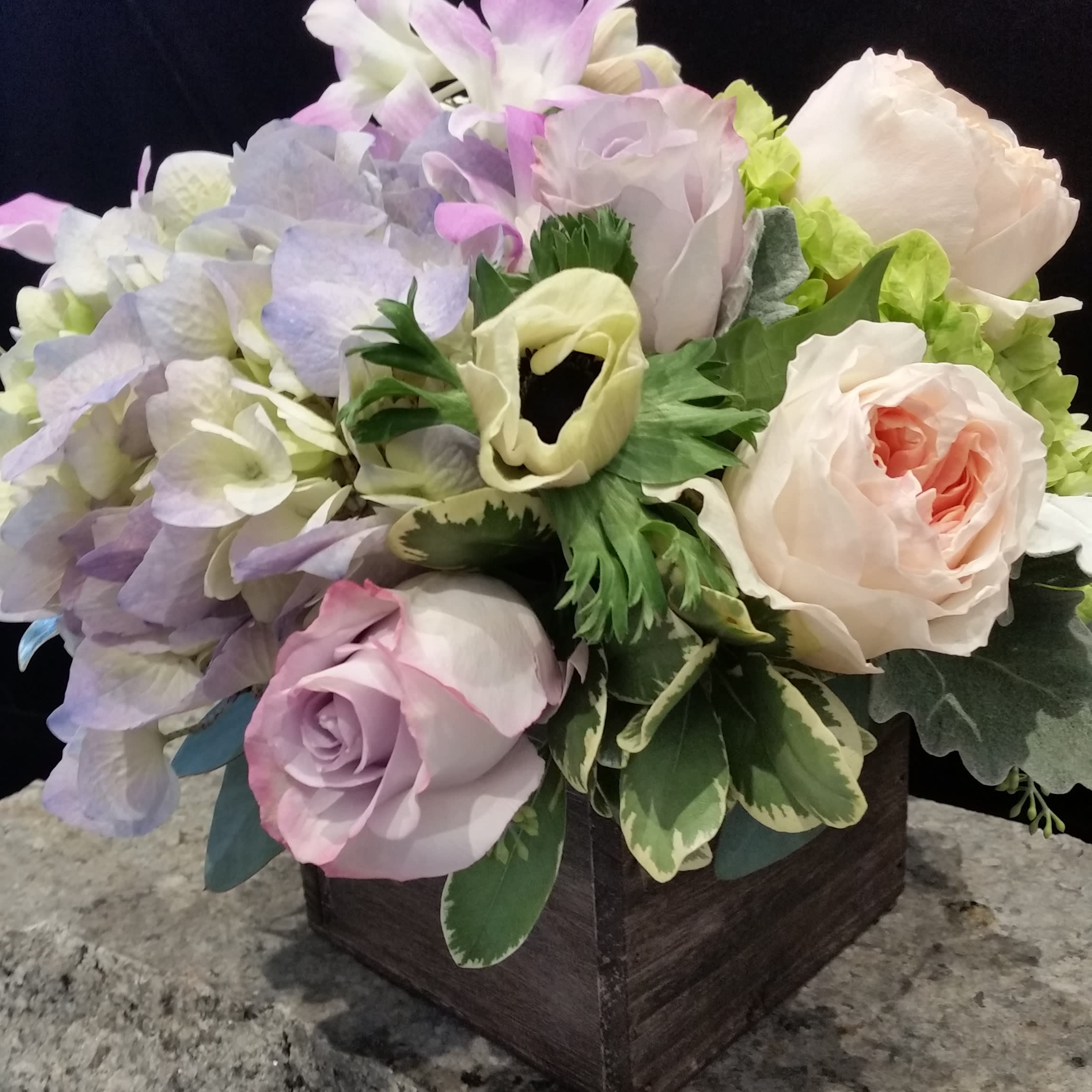A Walk in the Woods - We have featured an enchanting mix of soft colors and natural flowers in a simple wooden cube for this arrangement called A Walk in the Woods.  'Natural' is in style. A simple wooden cube contains lavender and cream hydrangea, premium lavender and peach roses, stunning peach garden roses, and white anemone. Uncomplicated and so very pretty!