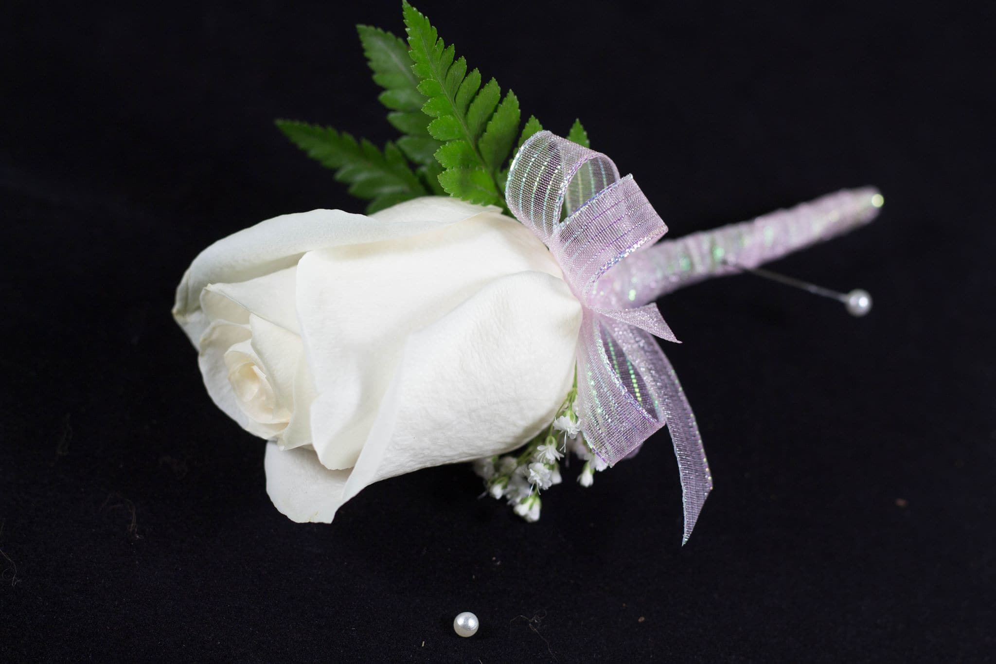 White rose boutonniere with a lavender ribbon and green fern