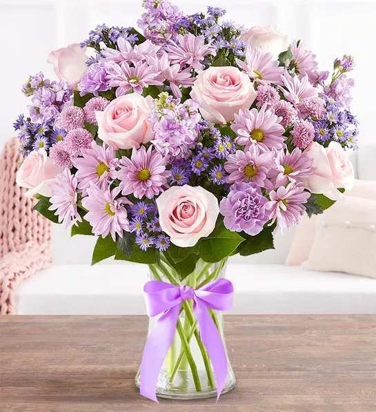 Pink and lavender bouquet of roses and daisies in a glass vase with a purple ribbon
