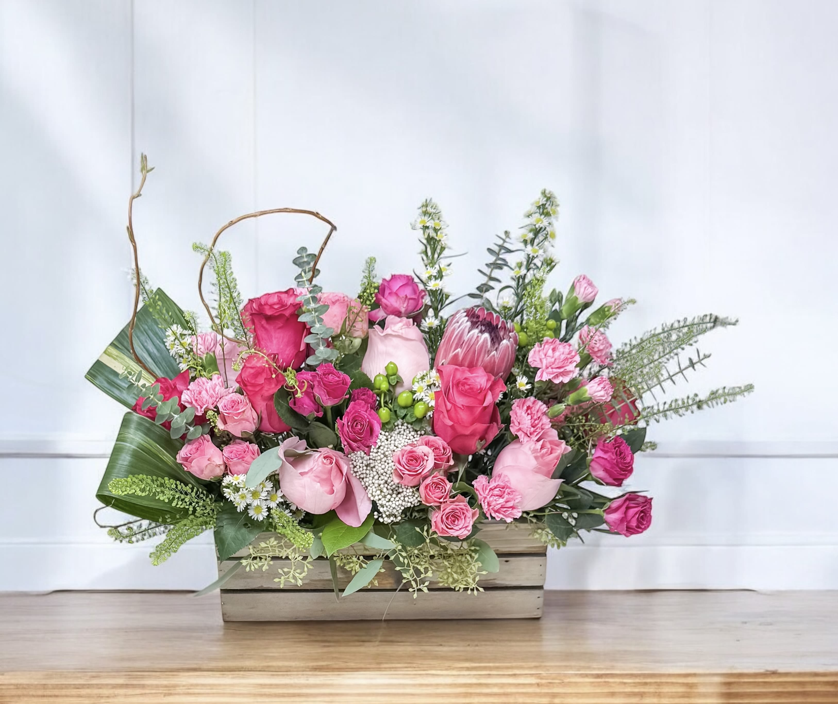 Pink rose and protea arrangement in a wooden box