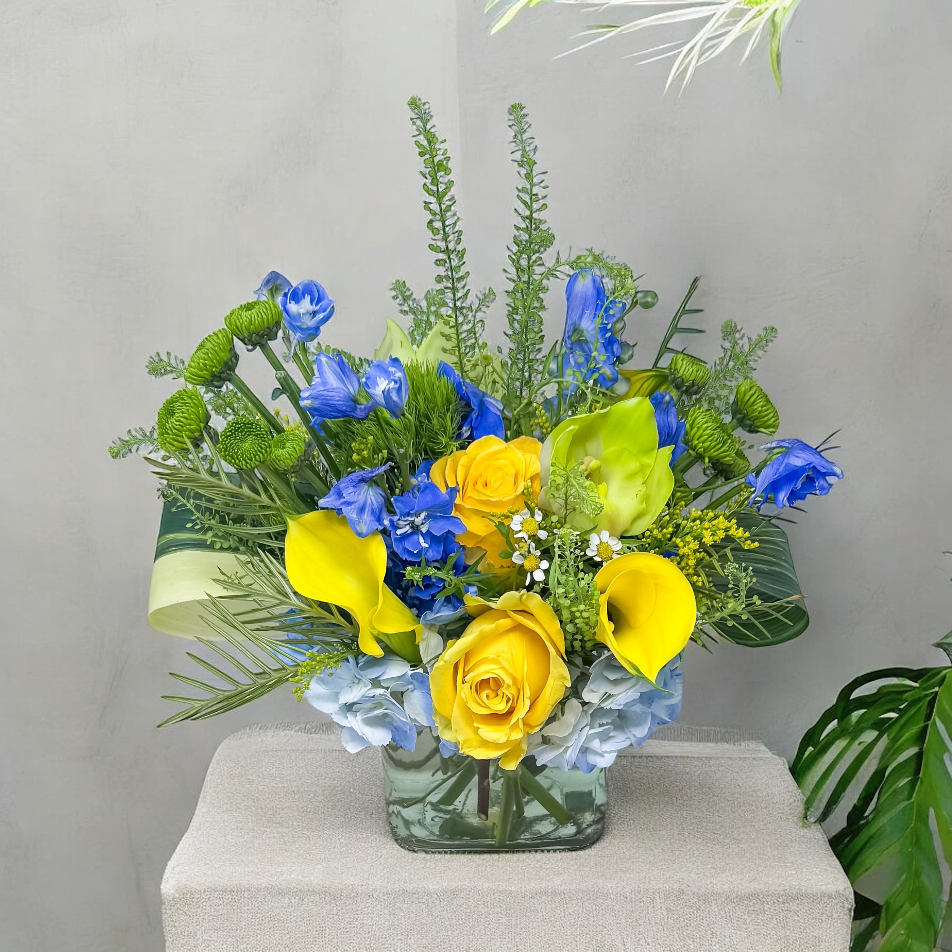 Blue and yellow floral arrangement in a square glass vase