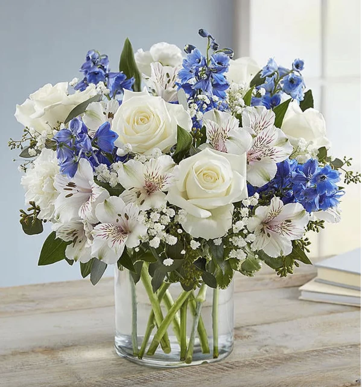 White roses and blue flowers arranged in a clear glass vase.