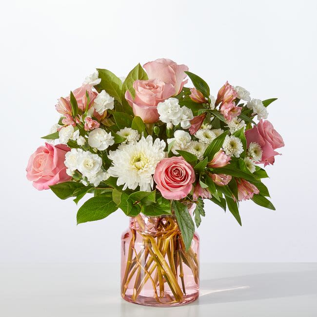 Pink roses and white daisies arranged in a pink glass vase