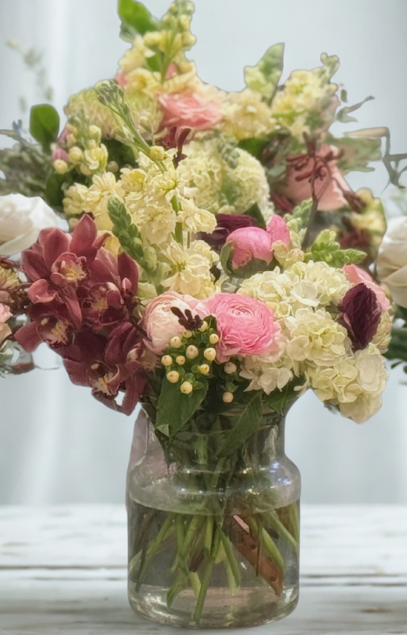 Mixed pink, cream, and burgundy flowers in a glass vase