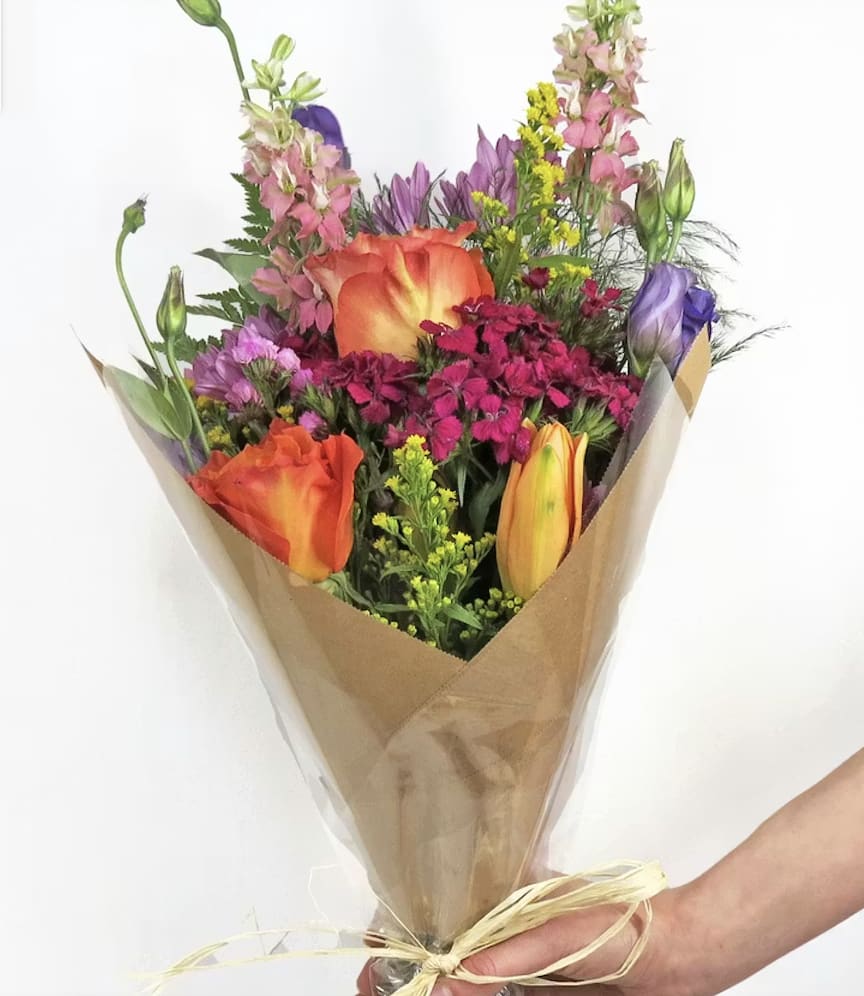 Mixed bouquet of orange, pink, purple, and yellow flowers wrapped in brown paper