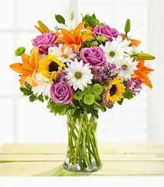 Mixed bouquet of orange lilies, purple roses, and white daisies in a glass vase