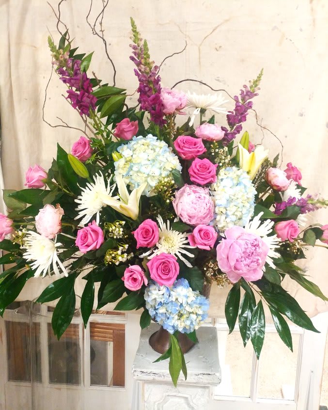 Large mixed floral arrangement with pink roses, blue hydrangeas, and white lilies in a vase.