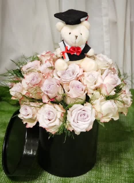 Teddy bear in a graduation cap sitting in a bouquet of pale pink roses