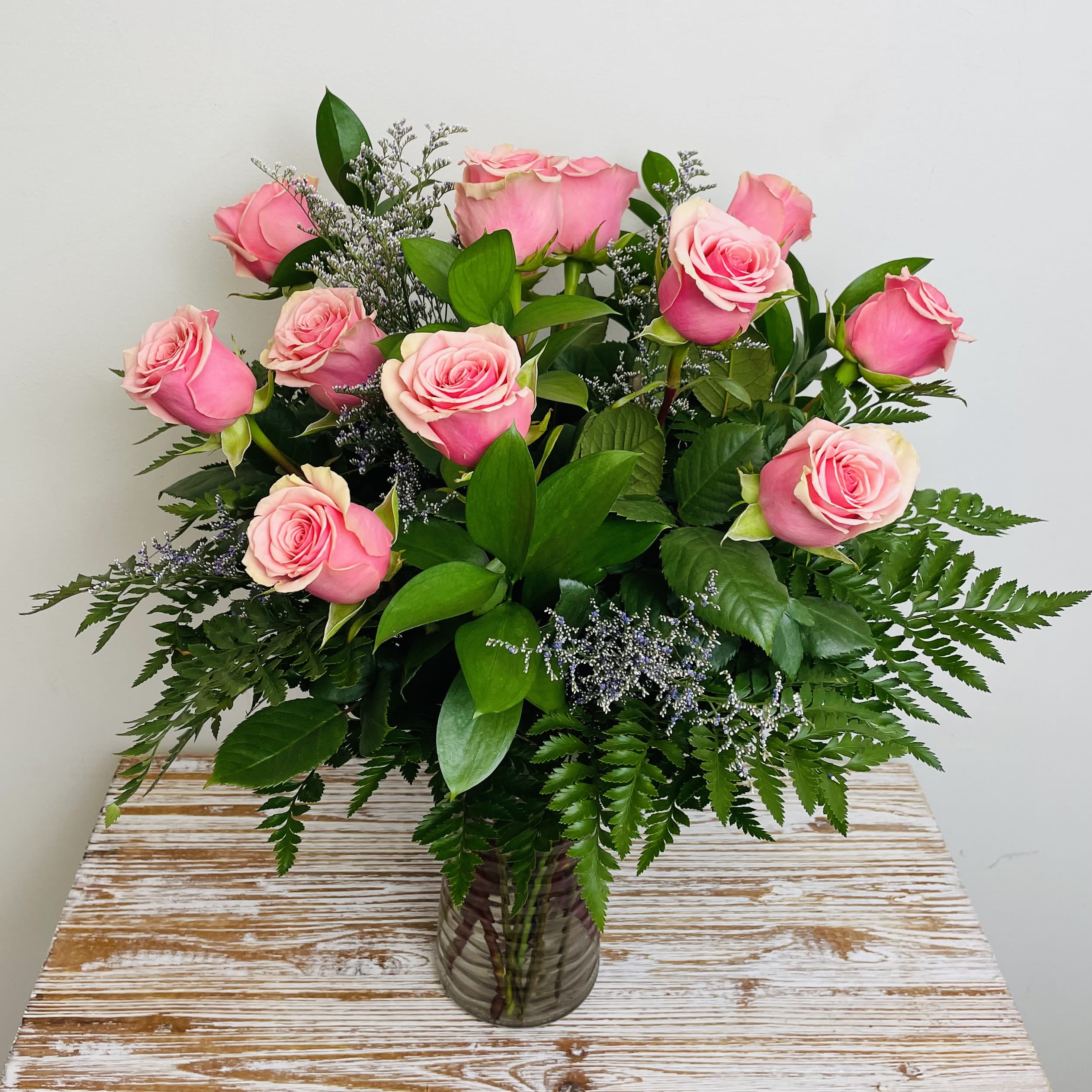 Pink roses arranged in a clear glass vase with greenery.