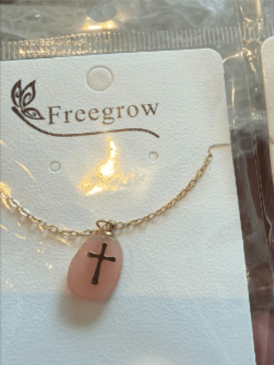 Stone Cross Necklace - A delicate gold-tone necklace with a soft pink oval pendant and a simple black cross makes a gentle, faith-forward gift that feels both personal and polished. Perfect as a Just Because keepsake, a birthday surprise, or a thank-you present, this necklace also suits Mother's Day or confirmation celebrations when you want the recipient to feel seen and supported.  The pendant's muted pink hue and clean black cross sit on a fine gold chain, presented on a white display card and tucked into clear plastic packaging for a tidy, retail-ready look. The minimal styling reads classic and versatile-easy to pair with everyday outfits-and the compact size makes it a wearable reminder rather than bold statement jewelry.  Give this as part of a small gift set or on its own to mark a quiet moment of appreciation; the recipient will enjoy a thoughtful, faith-based token they can wear daily. Care is simple: store on the card to avoid tangling and keep away from water and harsh chemicals to preserve the gold-tone finish.