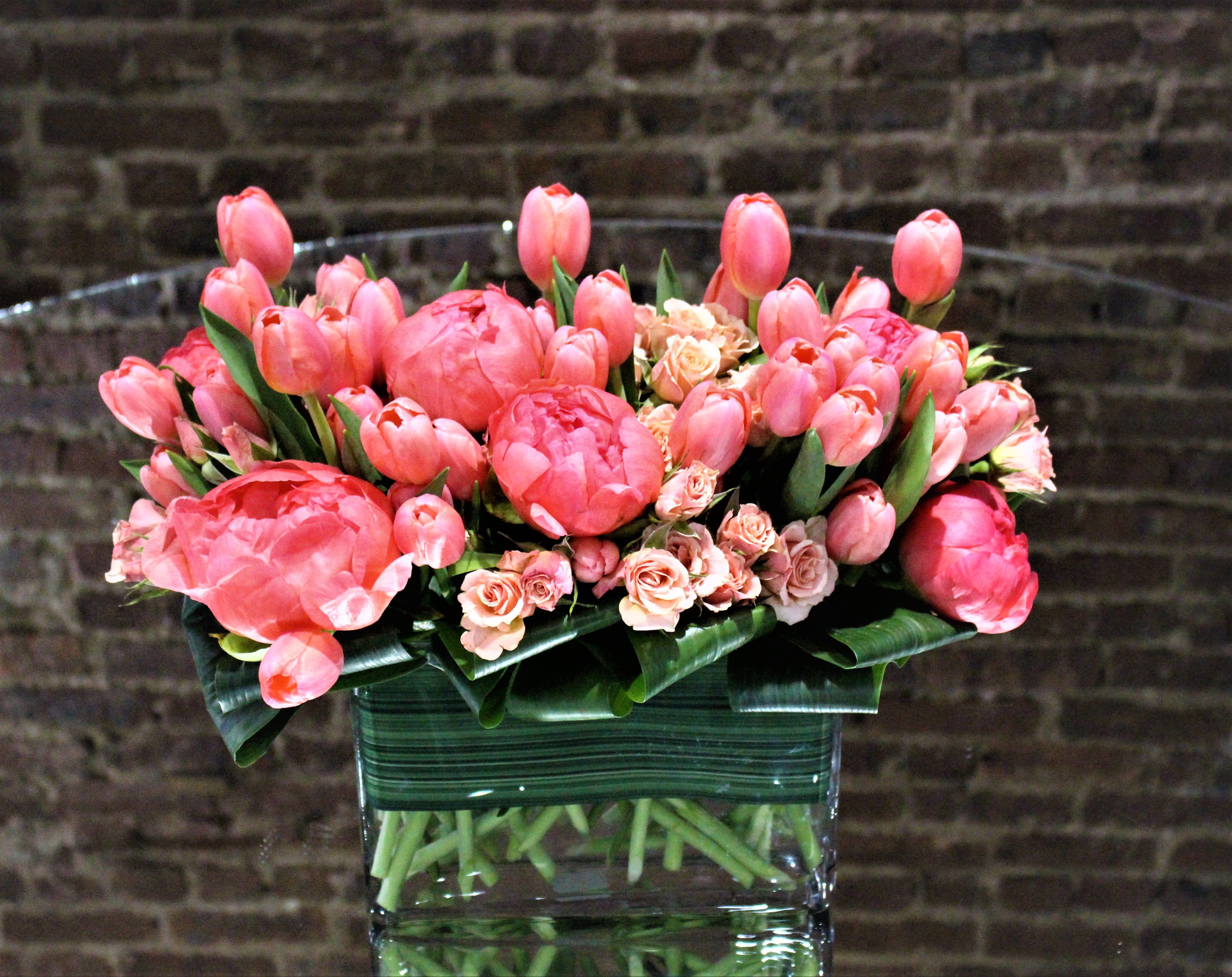 Pink tulips and small roses arranged in a clear glass vase