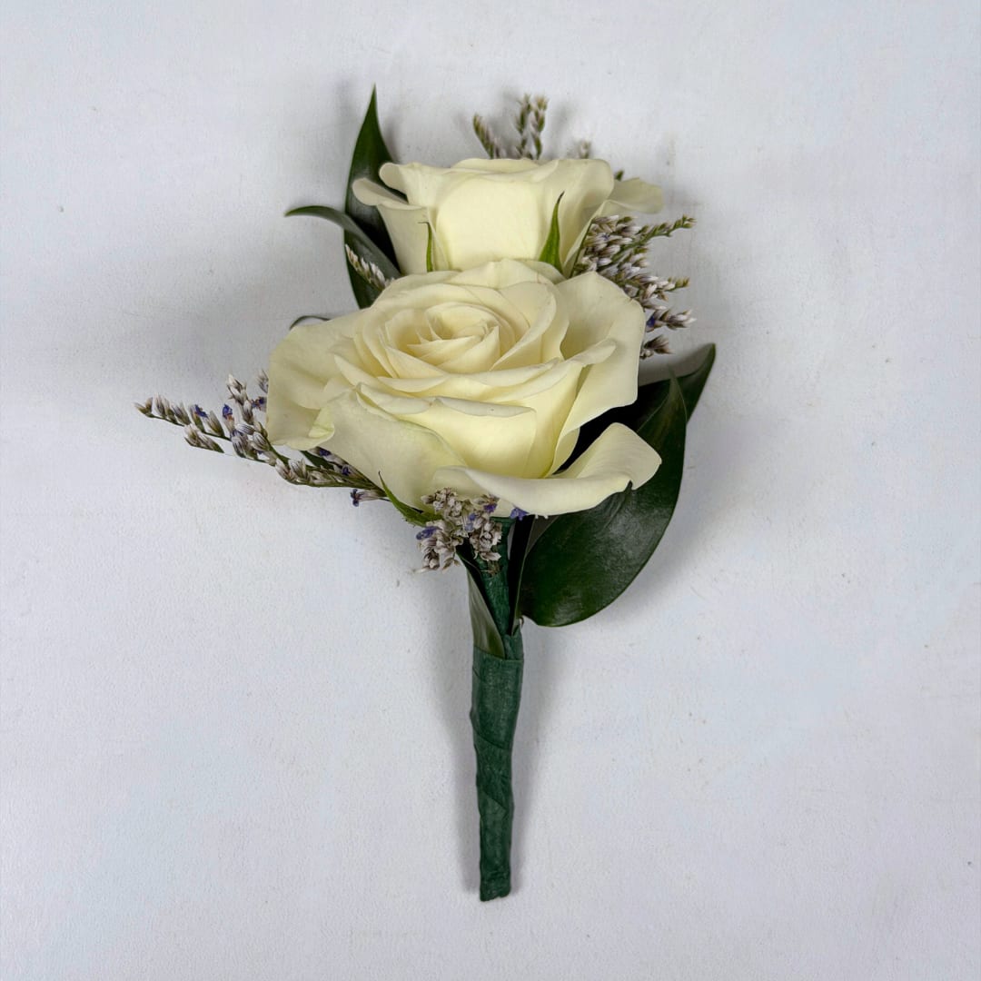 White Spray Rose Limonium Boutonniere - Two ivory-white spray roses are clustered tightly together in this white spray rose limonium boutonniere, creating an elegantly compact lapel piece perfect for weddings, proms, or any dressy occasion. The soft white palette and tiny limonium filler blooms give a quietly romantic impression, while the dark green leaves provide a crisp contrast that keeps the look classic and formal.  The boutonniere is finished with a neat, floral taped boutonniere wrap around the stem and a boutonniere pin to attach the boutonniere for a clean, structured silhouette that sits comfortably on a jacket or suit. The white spray roses are versatile and go with almost any outfit, making this a great choice all around no matter the color palette or occasion.   To jazz up this boutonniere even more, consider adding on a special ribbon wrap or even some sparkle accents so you can really dazzle on the dancefloor. To select your colors, check out our add-ons below or at checkout and pick whichever color you want.