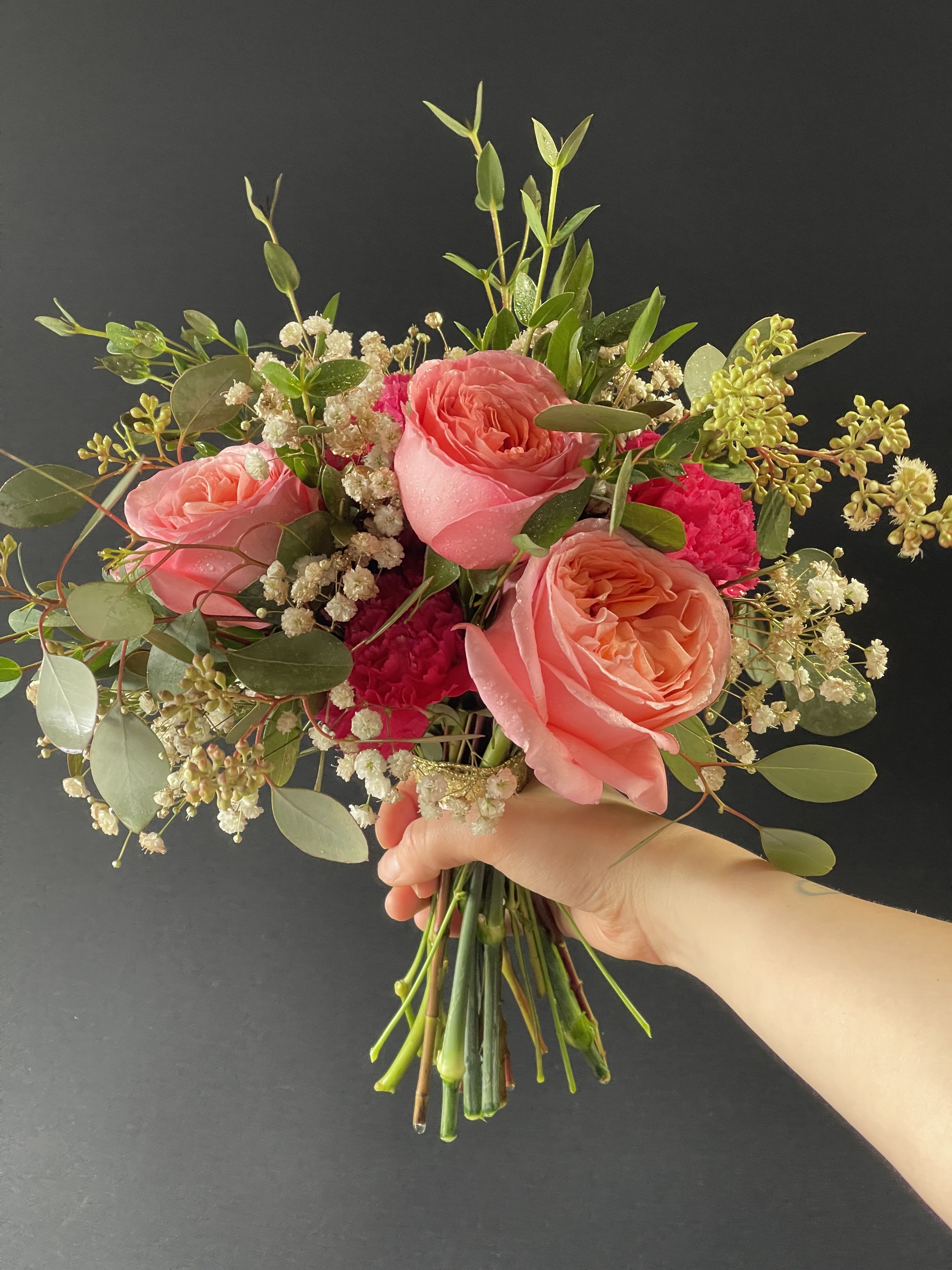 Hand-tied bouquet of coral roses with pink blooms and white filler flowers against a dark background.
