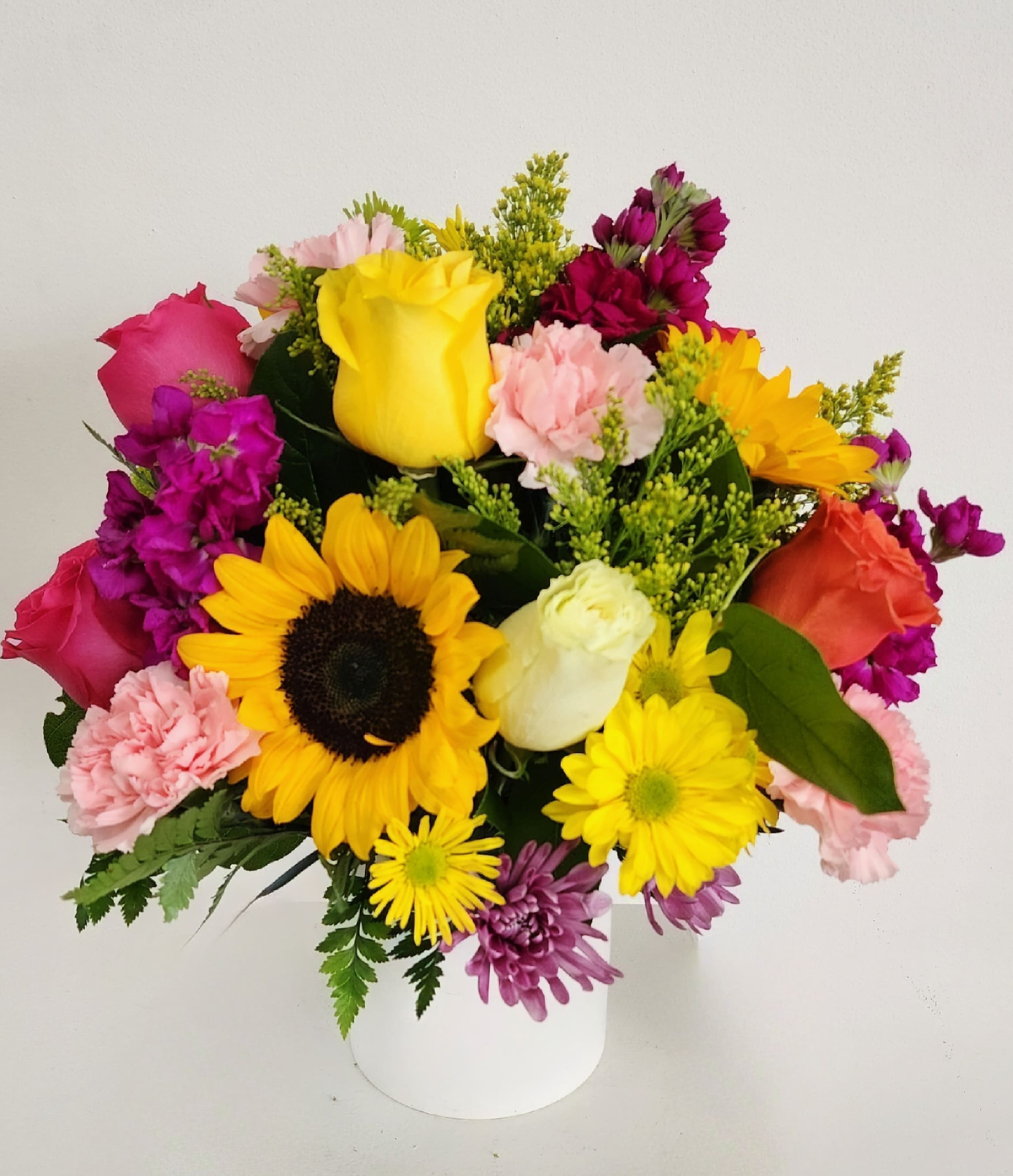 Mixed bouquet with sunflowers, roses, and carnations in a white vase