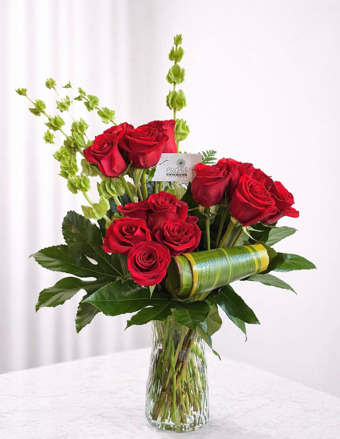 Velvet Devotion - Red roses...the ultimate symbol of deep love. This beautiful vase arrangement comes with 18 red roses, monstera leaves, and bells of Ireland flower.  