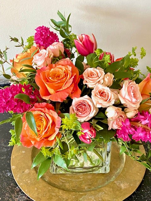 Mixed bouquet of orange and blush roses with pink blooms in a glass vase.