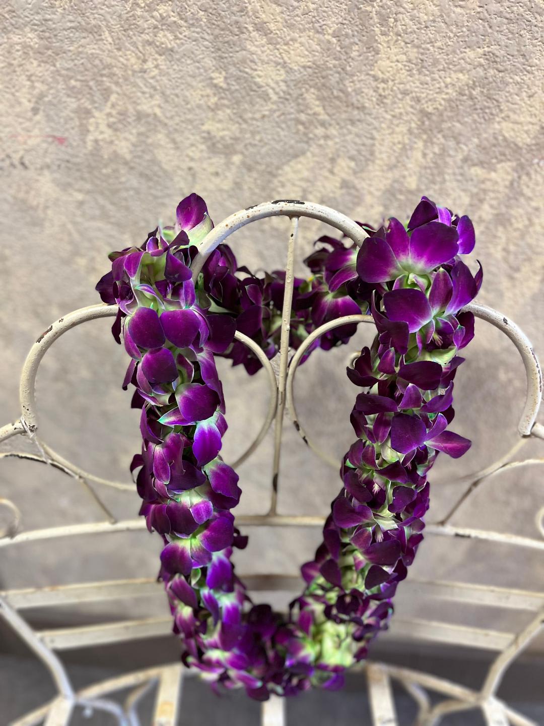 Purple orchid lei draped over a white metal chair