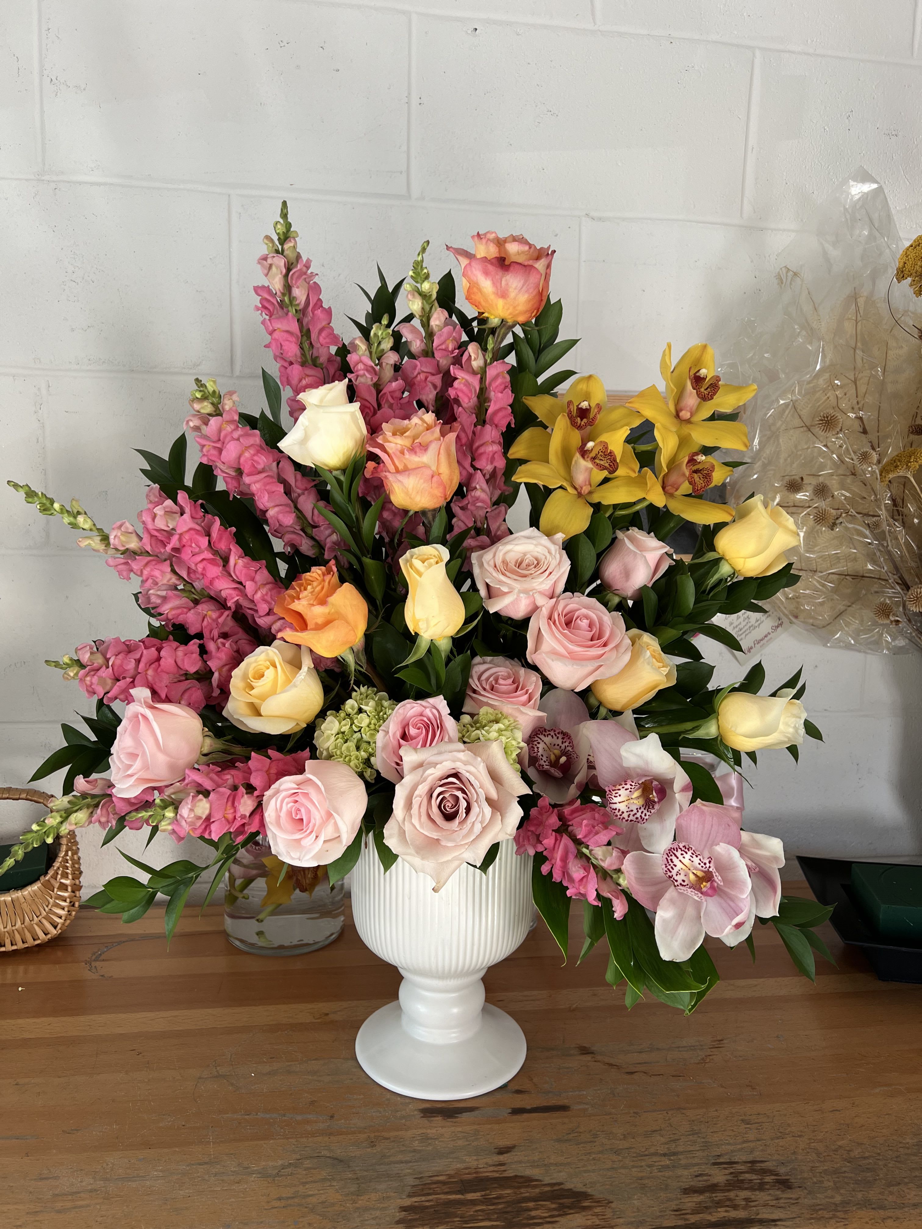 Mixed bouquet of pink, yellow, and peach flowers in a white vase.