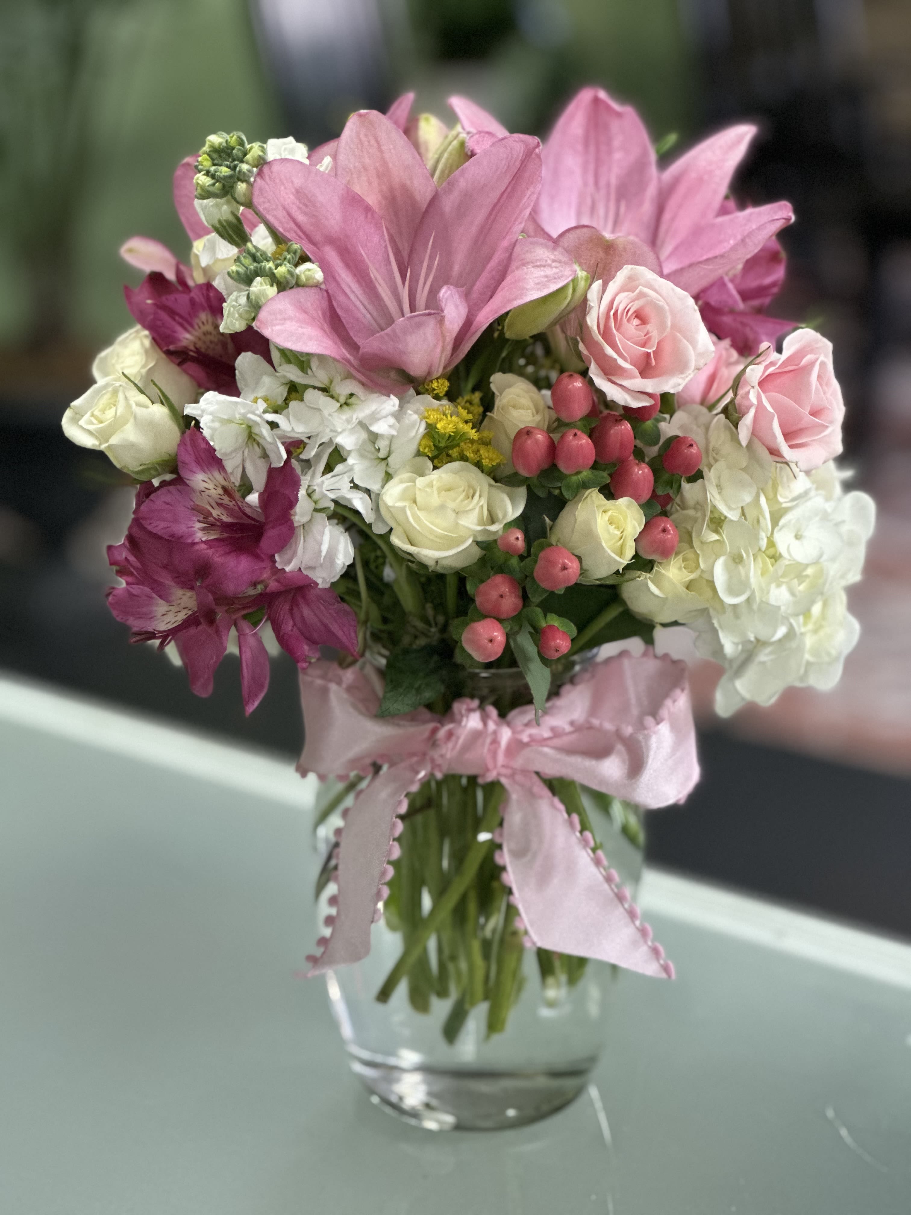 Pink and white mixed bouquet in a glass vase with a pink ribbon