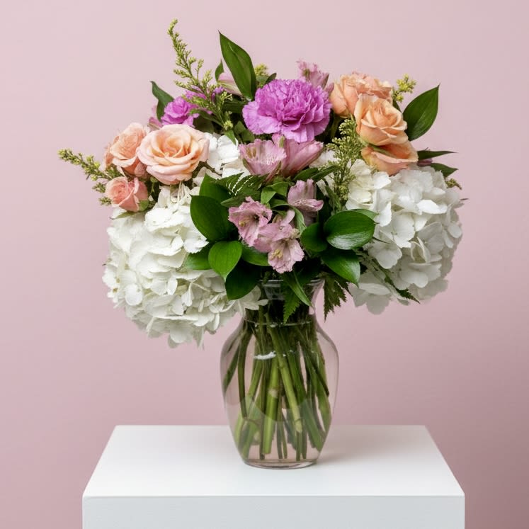 Blush &amp; Bloom for Mom - A soft and elegant Mother's Day arrangement designed in a clear glass vase, featuring lush white hydrangea accented with pink alstroemeria, peach spray roses, vibrant lavender carnations, and delicate seasonal fillers.