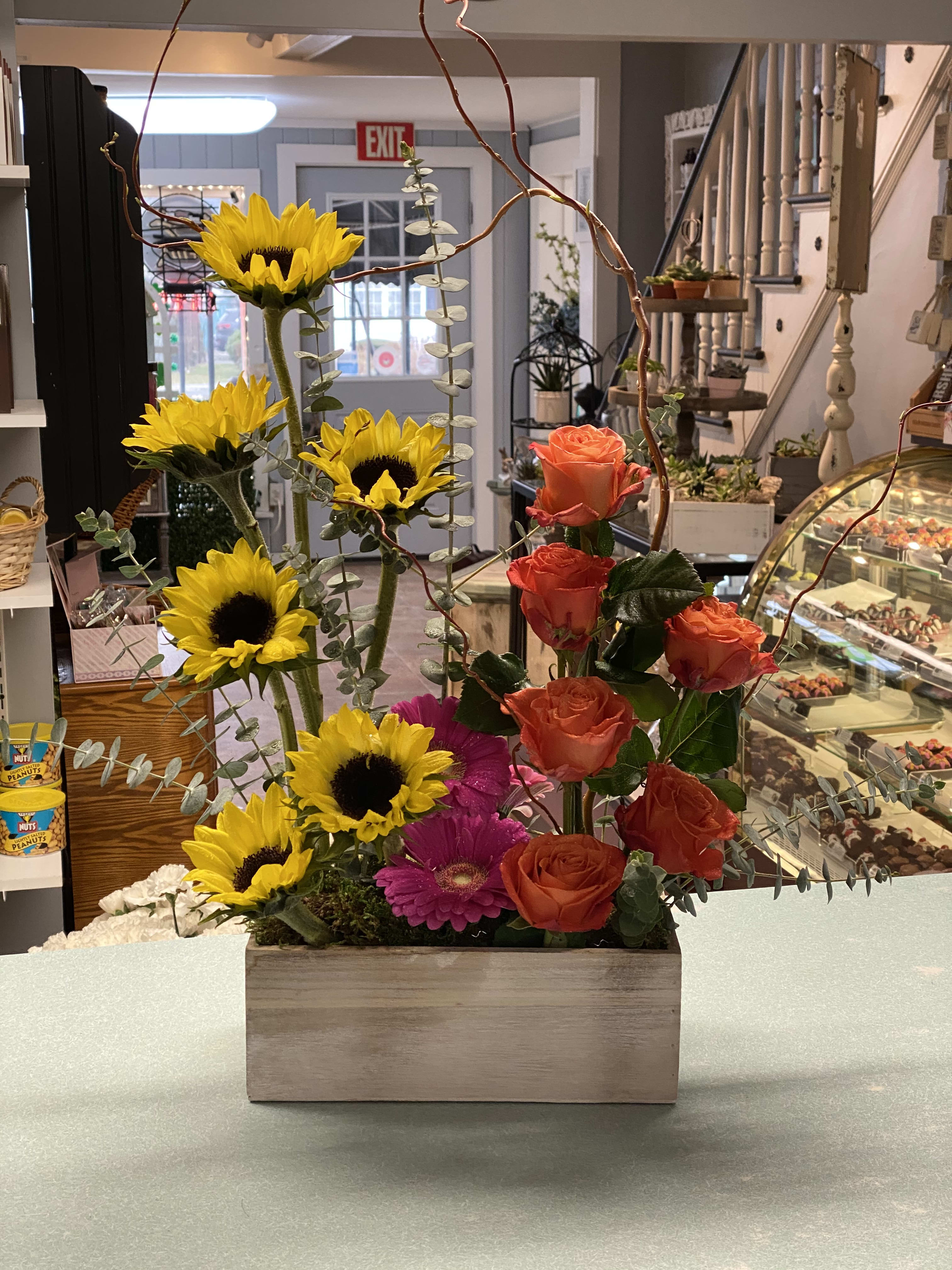 Mixed bouquet with sunflowers, orange roses, and pink gerbera daisies in a wooden box