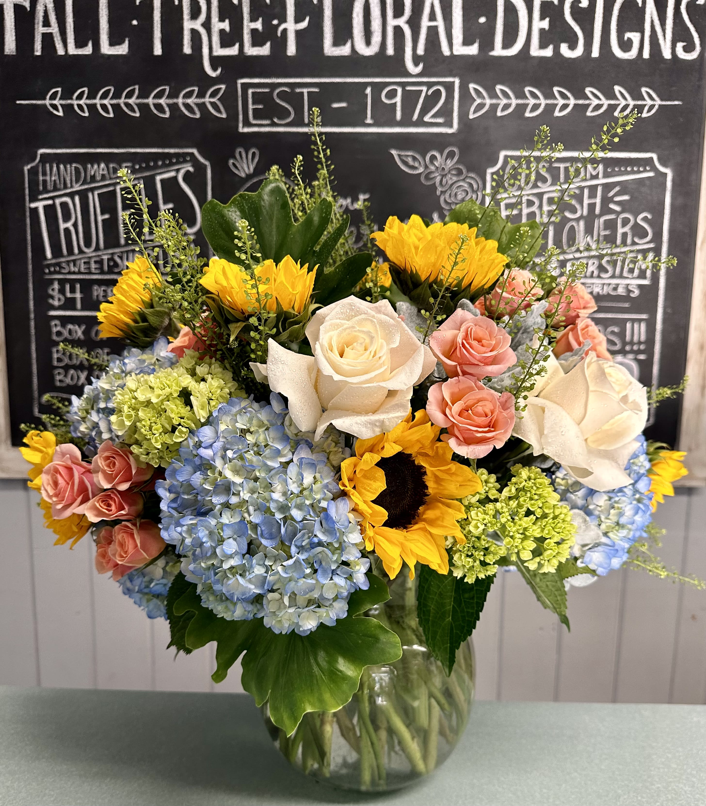 Mixed bouquet of sunflowers, roses, and hydrangeas in a glass vase