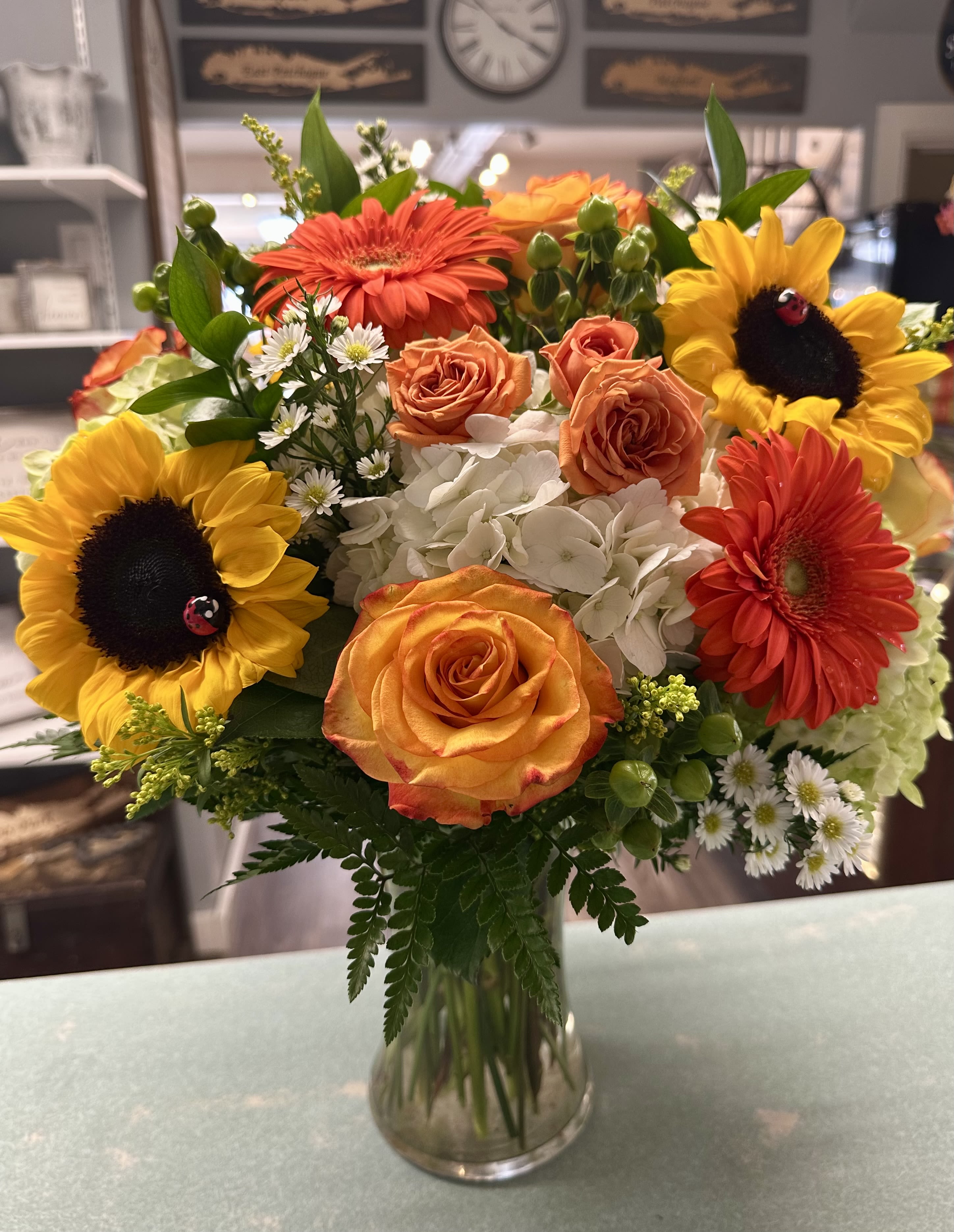 Bouquet of sunflowers, orange roses, and white hydrangeas in a glass vase