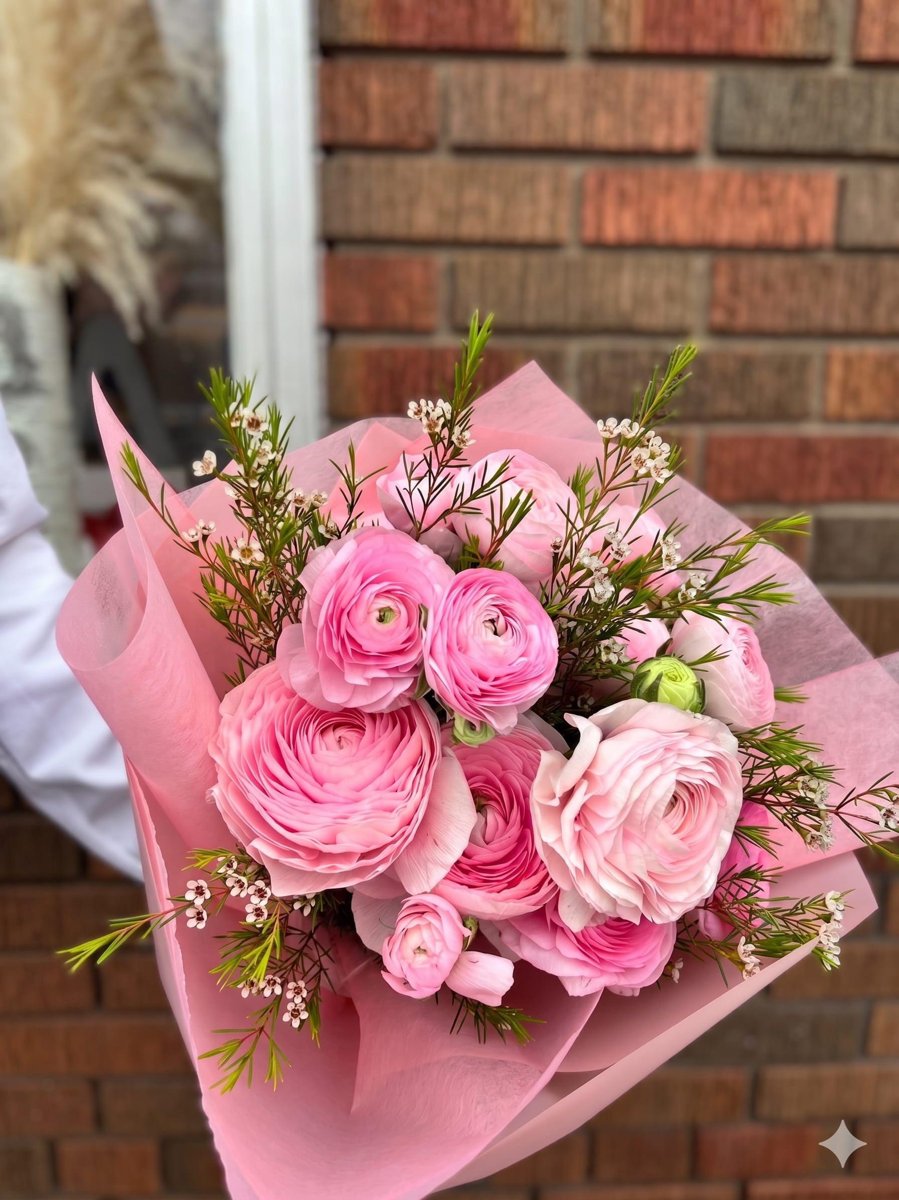 BP118 - The Pink Lindy - A luxurious, textured bouquet featuring a sweet melody of blushing pinks. This garden-style arrangement is packed with premium ranunculus and delicate waxflower blooms, accented with fine greenery. Wrapped elegantly in pink paper.  Seasonality: Ranunculus (available late winter/spring)