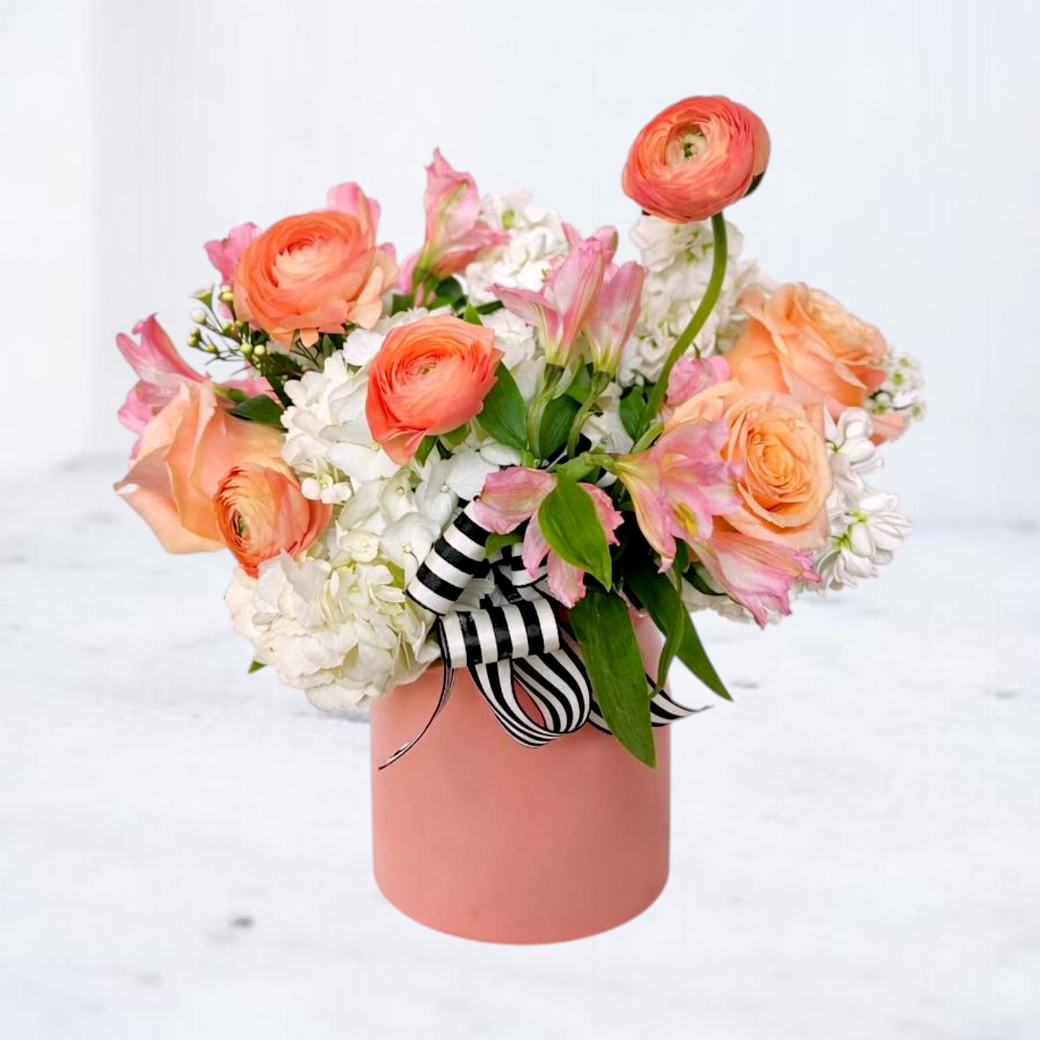 Marseille - Marseille is a modern floral arrangement featuring layered peach roses, ranunculus, and white hydrangea accented with soft pink blooms and fresh greenery. Designed in a contemporary vase with a striped ribbon detail, this piece blends warmth and structure for a polished, editorial look.  Perfect for birthdays, celebrations, or everyday delivery, Marseille offers a fresh take on soft, romantic color palettes without feeling overly traditional. Each arrangement is thoughtfully designed using premium seasonal flowers to create balance, movement, and texture.  Available for same-day flower delivery in Magnolia, TX and surrounding areas including The Woodlands, Montgomery, Conroe, and Spring. Designed by Whiskey Wallflower for those who want something elevated, intentional, and beautifully composed.