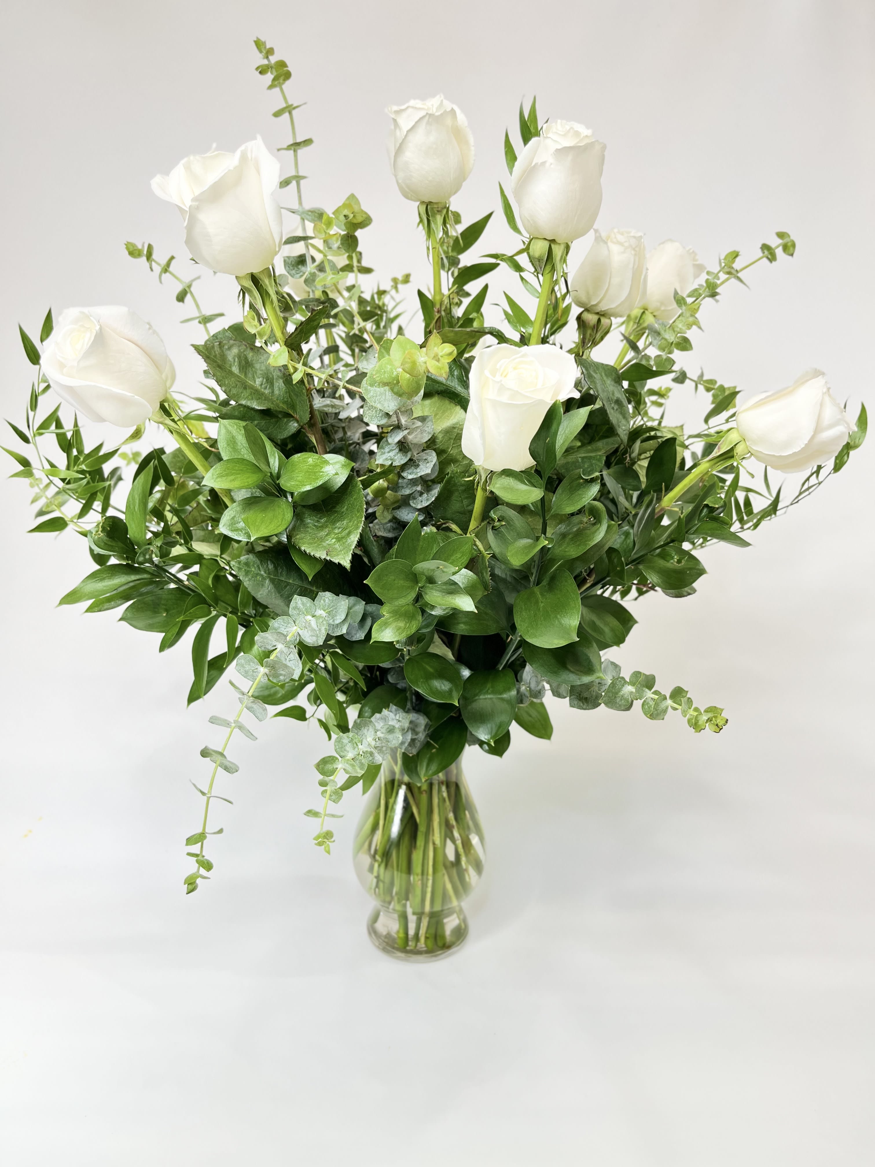 White roses arranged in a clear glass vase with greenery