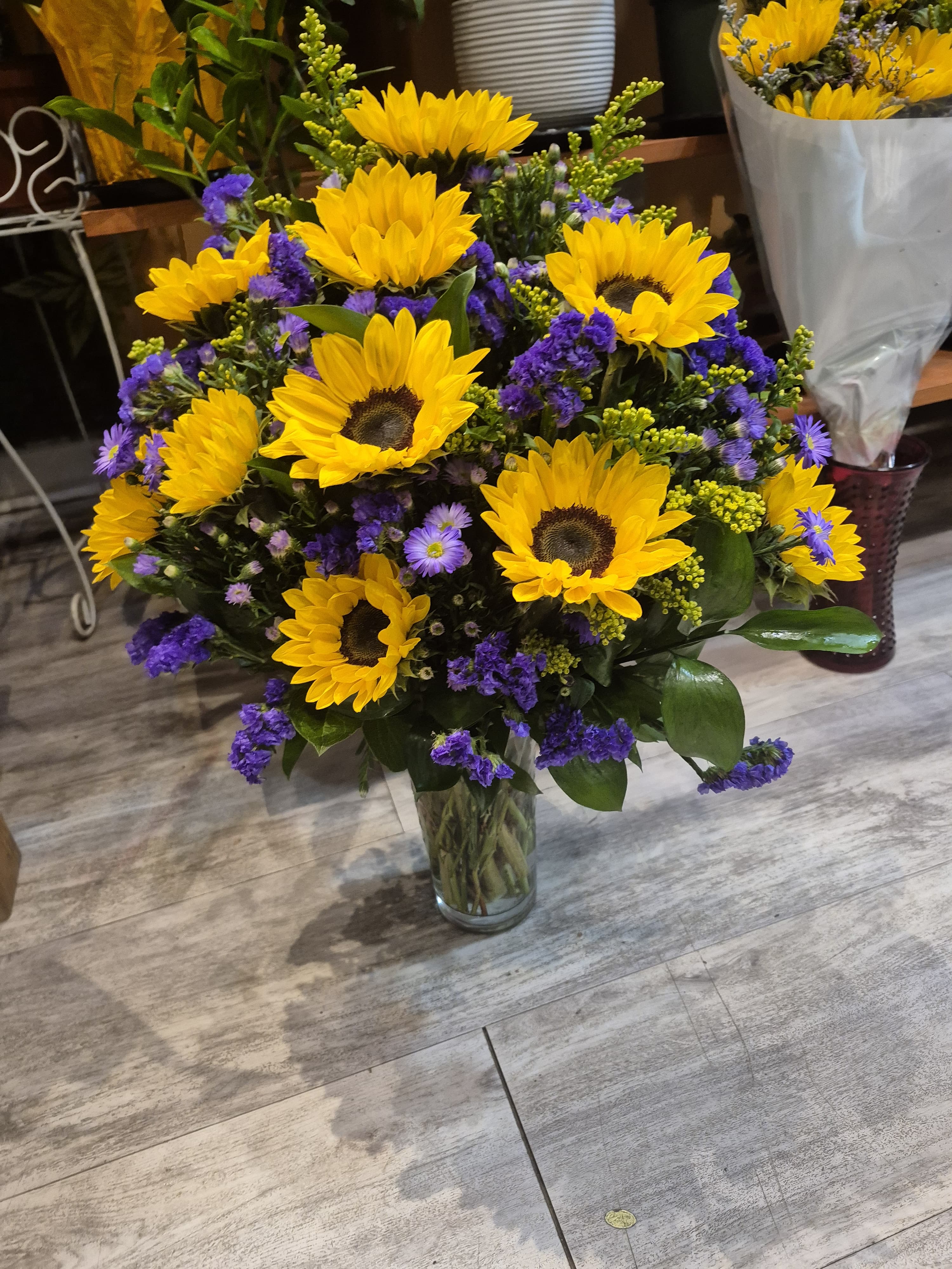 Bouquet of yellow sunflowers and purple filler flowers in a clear glass vase.